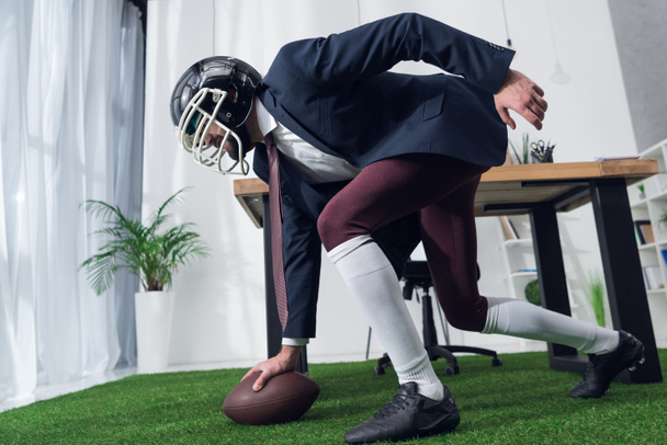 side view of businessman in rugby helmet playing american football in office - Foto, imagen