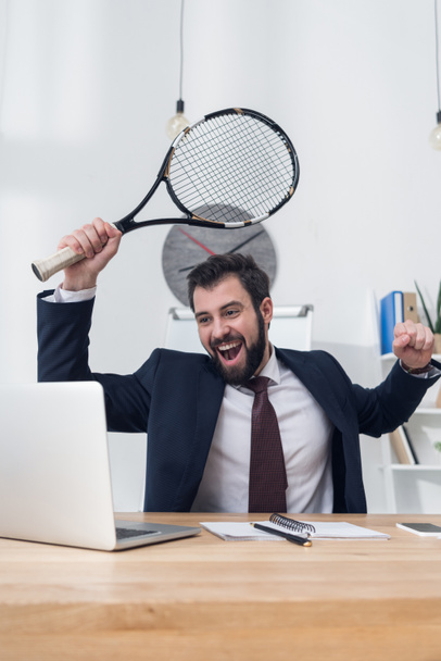 portrait of excited businessman in suit with tennis racket at workplace - Foto, afbeelding