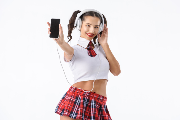 ヘッドフォンと白で隔離のスマート フォンで音楽を聴くセクシーな女子高生の笑顔 - 写真・画像