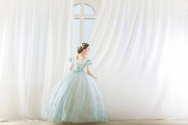 Elegante donna ad una finestra alta in abito storico, raddrizza le tende, e in attesa di amici al ballo di fine anno
 - Foto, immagini
