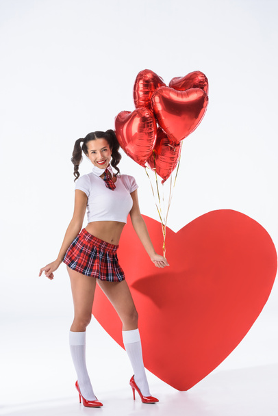 Młoda seksowna uczennica z helem balony w kształcie serc przed duże czerwone serce na białym - Zdjęcie, obraz