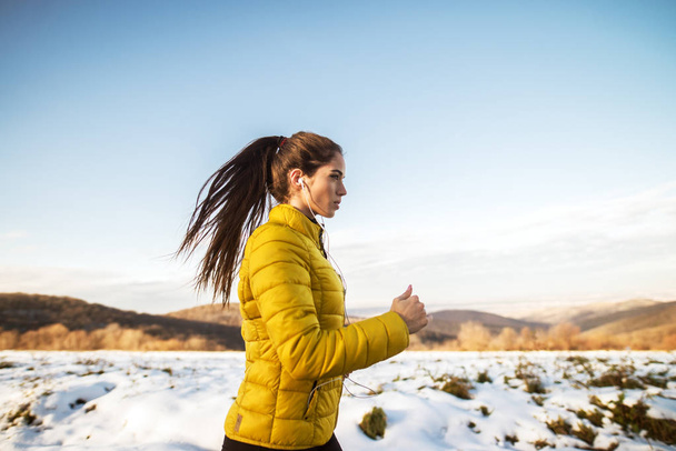 mujer joven y deportiva trotando en ropa deportiva de invierno con auriculares
 - Foto, Imagen