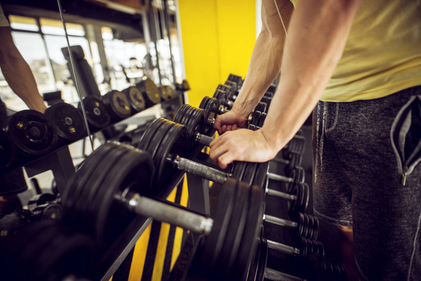 сильний м'язистий чоловік вибирає гантелі з ряду в спортзалі
 - Фото, зображення