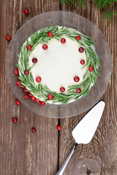 Homemade cake with cream cheese frosting, decorated with rosemary and berries on a wooden table - Фото, изображение