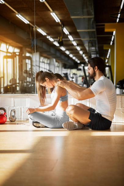 attractive couple sitting on the floor in gym. Man massaging his girlfriend - Photo, Image