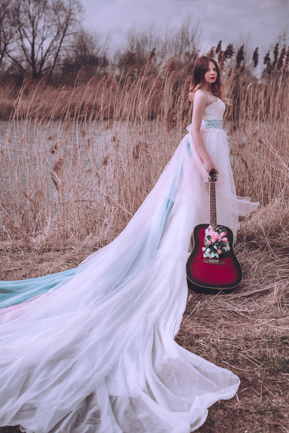 Menina europeia romântica bonita com guitarra com flores dentro, posando ao ar livre. Conceito de música e natureza. Hora da Primavera
. - Foto, Imagem