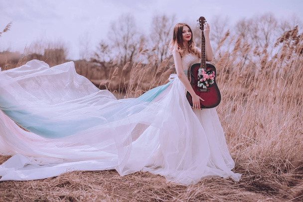Beautiful romantic european girl with guitar with flowers inside, posing outdoors. Concept of music and nature. Spring time. - Photo, Image