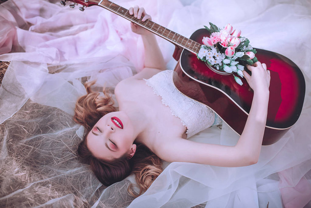 Belle fille romantique européenne avec guitare avec des fleurs à l'intérieur, posant à l'extérieur. Concept de musique et de nature. Printemps
. - Photo, image