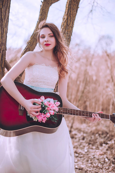 Όμορφη ρομαντική ευρωπαϊκή κοπέλα με κιθάρα με λουλούδια στο εσωτερικό, ποζάροντας σε εξωτερικούς χώρους. Έννοια της μουσικής και της φύσης. Άνοιξη. - Φωτογραφία, εικόνα