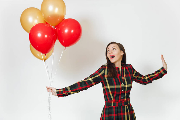 Beautiful caucasian young happy woman in long plaid checkered dress with shy charming smile, red, yellow golden balloons, celebrating birthday, on white background isolated. Holiday, party concept. - Φωτογραφία, εικόνα
