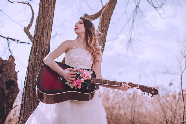 Krásná romantická evropská dívka s kytarou s květinami uvnitř, pózující venku. Pojem hudba a příroda. Jarní čas. - Fotografie, Obrázek