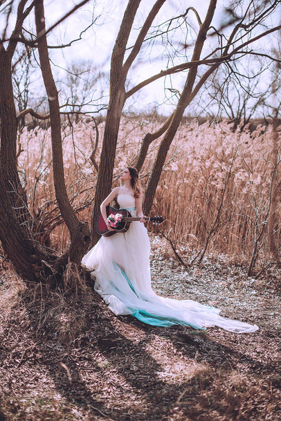 Menina europeia romântica bonita com guitarra com flores dentro, posando ao ar livre. Conceito de música e natureza. Hora da Primavera
. - Foto, Imagem