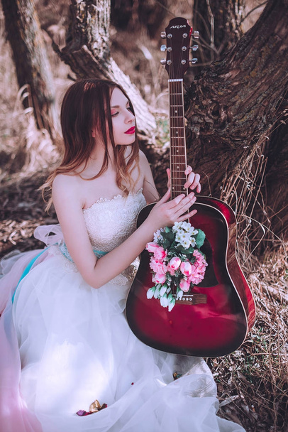 Schöne romantische europäische Mädchen mit Gitarre mit Blumen drinnen, posiert draußen. Konzept von Musik und Natur. Frühlingszeit. - Foto, Bild