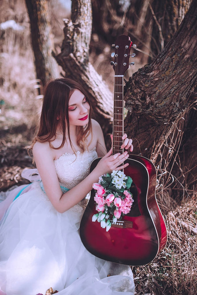 Όμορφη ρομαντική ευρωπαϊκή κοπέλα με κιθάρα με λουλούδια στο εσωτερικό, ποζάροντας σε εξωτερικούς χώρους. Έννοια της μουσικής και της φύσης. Άνοιξη. - Φωτογραφία, εικόνα