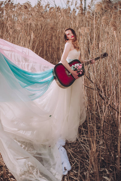 Hermosa chica romántica europea con guitarra con flores en el interior, posando al aire libre. Concepto de música y naturaleza. Primavera
. - Foto, Imagen