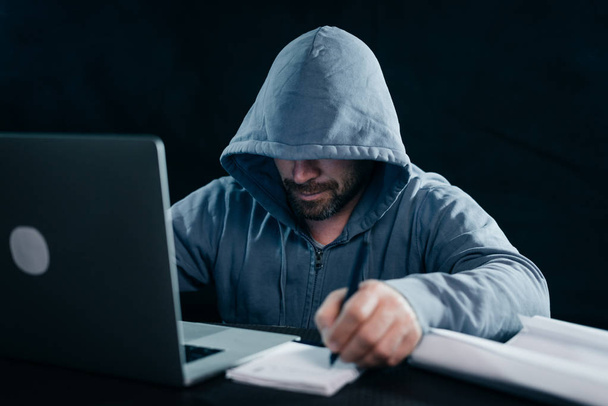 a secretive criminal man, hides his face, a hacker, writes something - Photo, Image