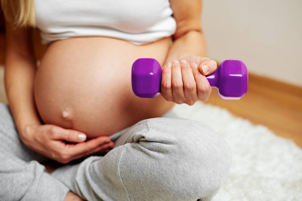 Zwangere vrouw met naakte buik trainen thuis. Gezondheid en lichaam care concept. - Foto, afbeelding