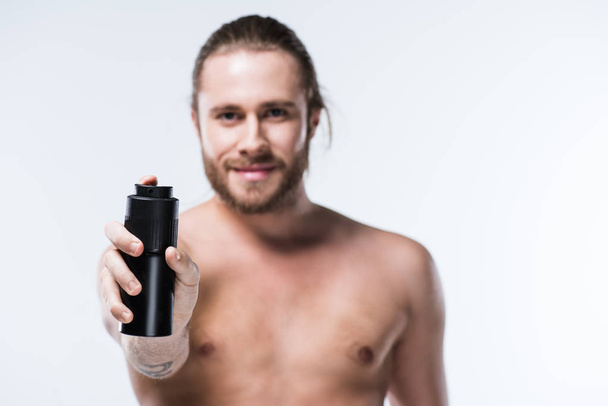 Cheerful young man holding deodorant spray in outstretched hand  - Фото, изображение