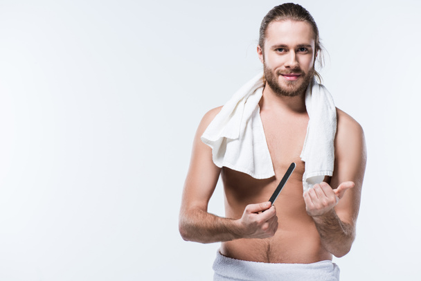 Joven guapo con toalla de baño alrededor de su cuello sosteniendo una lima de uñas, aislado en blanco
  - Foto, imagen