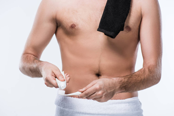 Midsection άνδρα με μαύρο πετσέτα στον ώμο και οδοντόκρεμα και οδοντόβουρτσα στα χέρια, απομονώνονται σε λευκό - Φωτογραφία, εικόνα