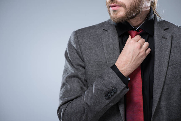 Imagen recortada del hombre de negocios barbudo tocando su corbata roja, aislado en gris
 - Foto, imagen