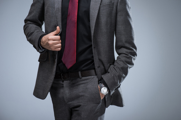 Cropped image of businessman holding side of jacket and hand in pocket, isolated on gray - Foto, afbeelding