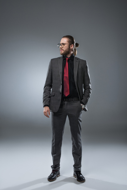 Businessman in glasses looking away with hand in pocket of jacket, isolated on gray - Photo, Image