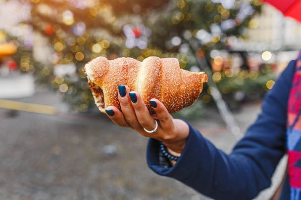 A woman with an appetite eats a traditional sweet pastry of Czech in Prague - a trdelnik on the background of a Christmas tree and a New Year's fair - Photo, image
