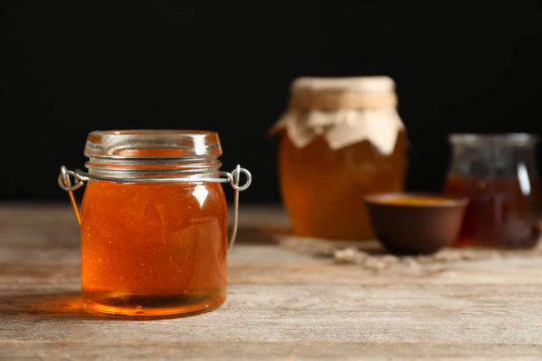 Glass jar with honey on wooden table - Valokuva, kuva