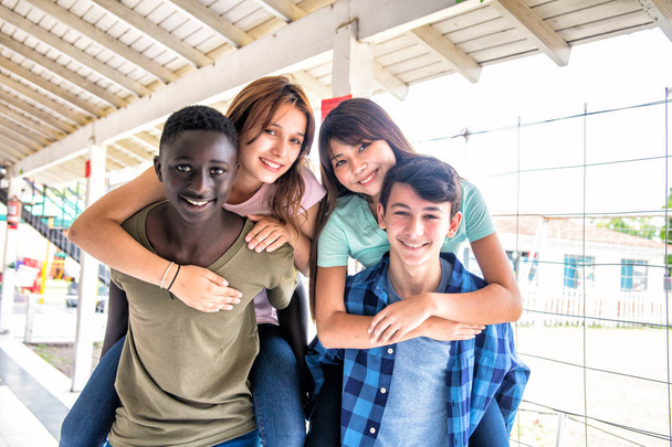 Two couples of mixed races teenagers playing piggyback at achool - Photo, Image
