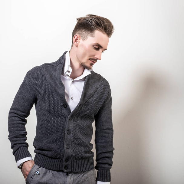 Handsome young elegant man in grey switer pose against studio background. - Fotó, kép