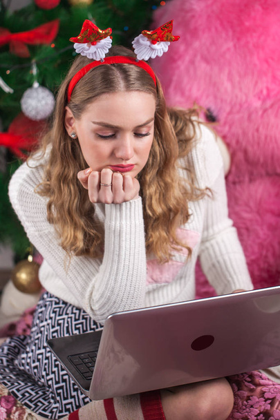 Menina blunde bonita usando laptop sentado no travesseiro. Inverno
 - Foto, Imagem