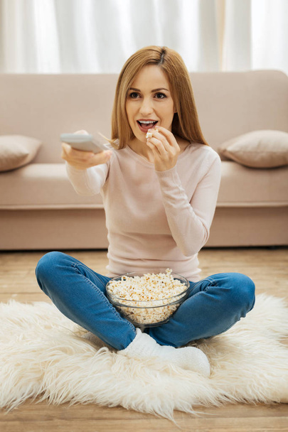 Smiling woman sitting on the carpet with popcorn - Zdjęcie, obraz