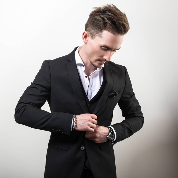 Handsome young elegant man in black stylish classic costume pose against studio background. - Foto, afbeelding