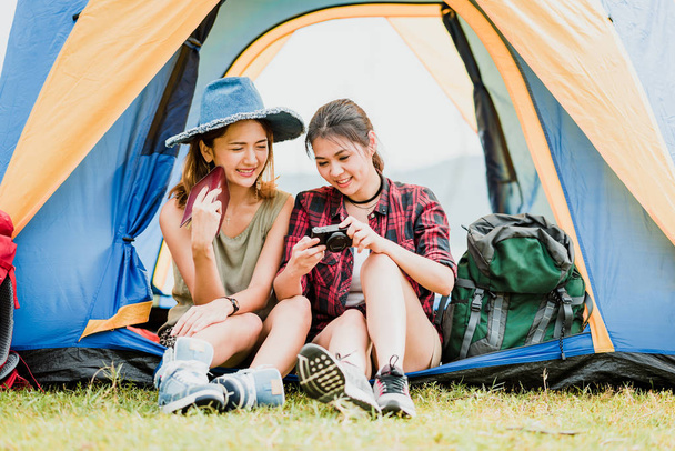 İki mutlu Asyalı kadın backpackers onların fotoğraf makinesindeki bir çadırın dışında tatil gezisi sırasında kontrol. - Fotoğraf, Görsel