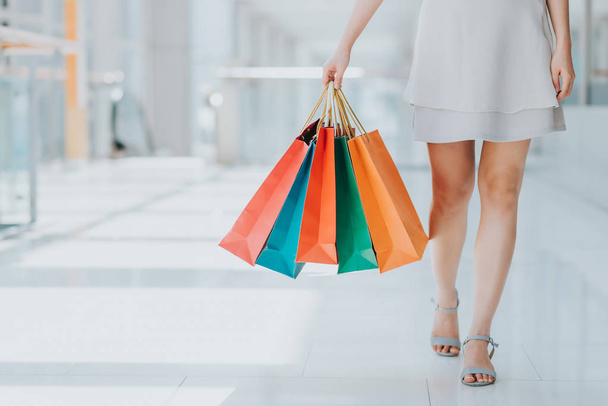 Alışveriş merkezinde yürürken renkli alışveriş çantaları taşırken genç kadın bacak görüntüsünü kapatmak - Fotoğraf, Görsel