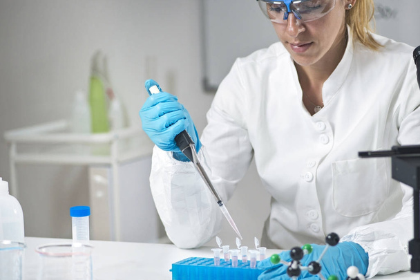 Young female scientist holding pipette in the lab wearing protective equipment - Фото, изображение