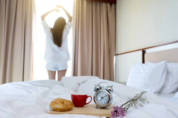 Молодая женщина в белой рубашке встает из постели в утреннее время с быстрым перерывом в спальне
 - Фото, изображение