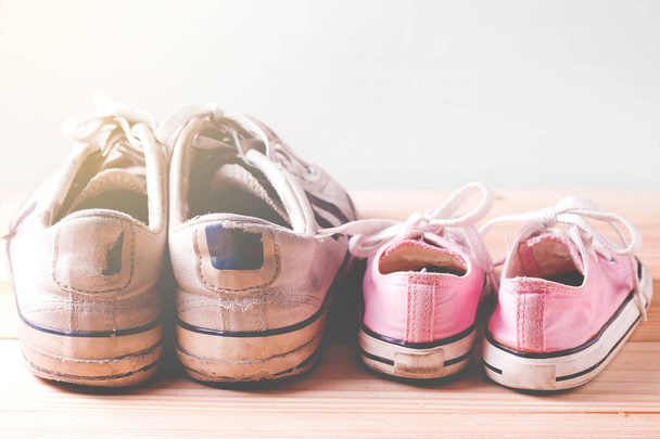Zapatillas niña rosa y zapatillas hombre blanco en un piso de madera y fondo blanco con espacio para copiar
 - Foto, imagen