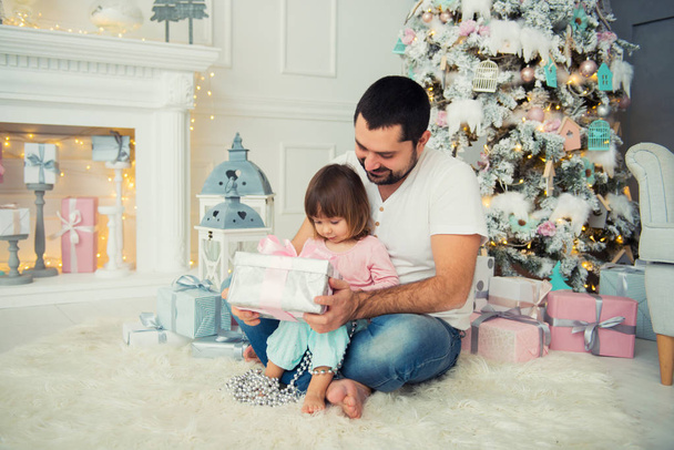 Big father and happy little daughter open New Years gifts near the Christmas tree - Foto, Imagem