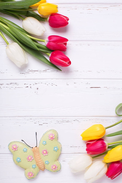 Frame from bright yellow, pink  and white tulips flowers  and decorative butterfly on  vintage wooden background. Selective focus. Place for text. - Foto, imagen
