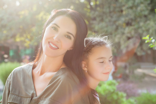 Young mother and cute girl sitting back to back in nature in sunlight - Photo, image