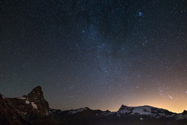 Wonderful starry sky over Matterhorn (Cervino) mountain peak and Monte Rosa glaciers, famous ski resort in Aosta Valley, Italy. Andromeda galaxy clearly visibile mid frame. - Foto, Bild