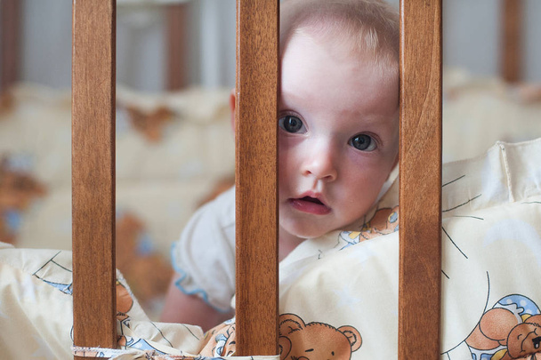 Cute smiling baby looking out of the crib. Funny kid in bed. Close up portrait - Fotografie, Obrázek