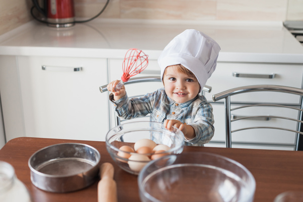 очаровательный маленький ребенок в шляпе шеф-повара с венчиком и яйцами
 - Фото, изображение