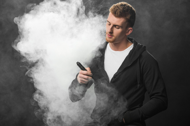 Jeune homme barbu fumant cigarette électronique entourée de nuages de vapeur
 - Photo, image