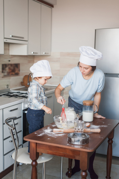 mother and adorable little child mixing dough with whisk at kitchen - Photo, Image