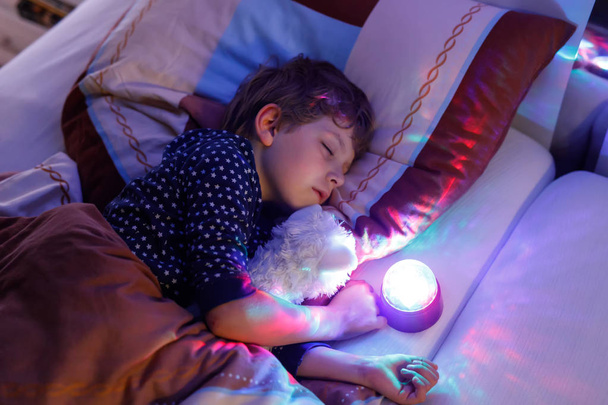 Μικρό αγόρι προσχολικής ηλικίας το παιδί κοιμάται στο κρεβάτι με πολύχρωμα λάμπα. - Φωτογραφία, εικόνα