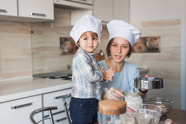 Schöne junge Mutter und Kind bereiten gemeinsam in der Küche Teig für Plätzchen zu - Foto, Bild