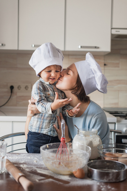 мать целует своего ребенка, пока они готовят тесто на кухне
 - Фото, изображение